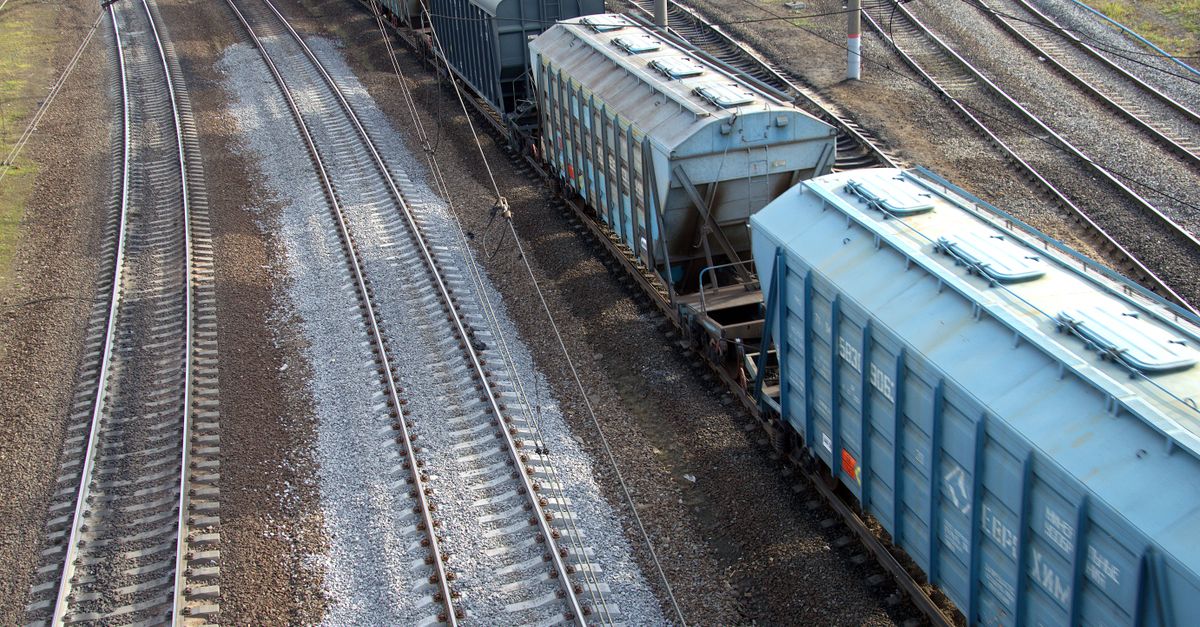Aerial perspective capturing a freight train on intersecting railway tracks during the day.
